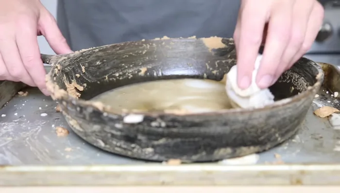 Let the baking soda paste sit for a few minutes, then add vinegar. Vinegar helps remove old seasoning.